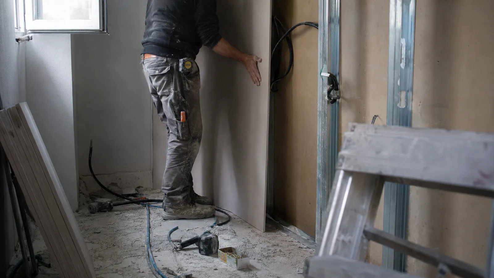 Artisan posant une plaque de plâtre sur un chantier de rénovation intérieure